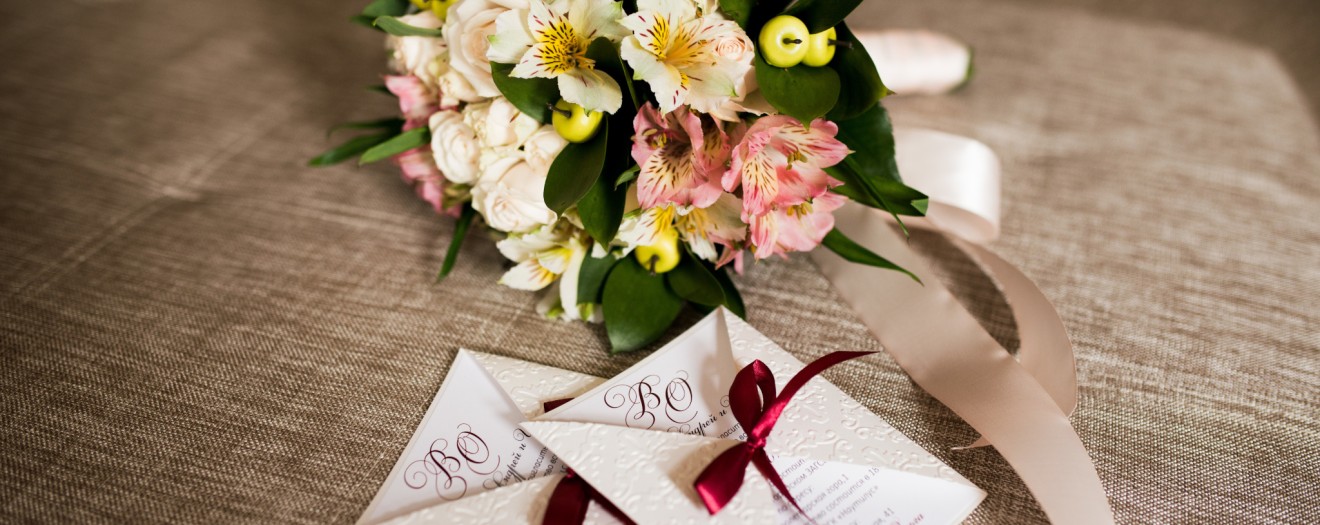 Zwei Einladungskarten für Hochzeit mit daneben liegenden Blumenstrauß