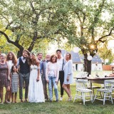Bride, groom, guests posing for the photo at wedding reception outside in the backyard.