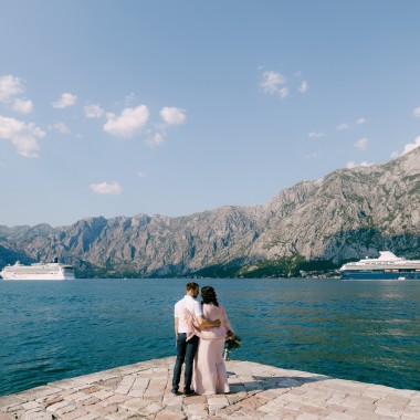 Bride and groom hug on the pier against the backdrop of liners and mountains. Back view