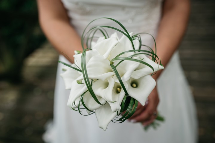 Braut hält einen eleganten Strauß aus weißen Calla-Lilien, umwickelt mit dekorativem Grün.