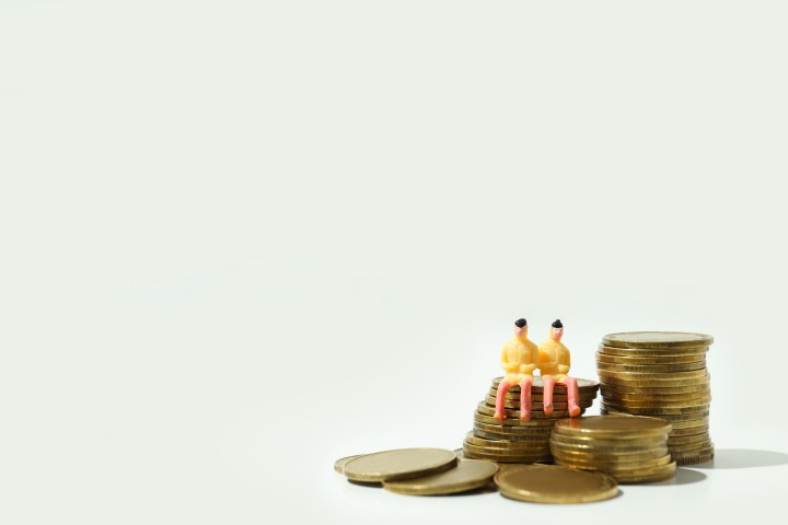 Zwei kleine Figuren sitzen auf gestapelten Münzen – Symbolbild für gemeinsames Sparen als Paar.