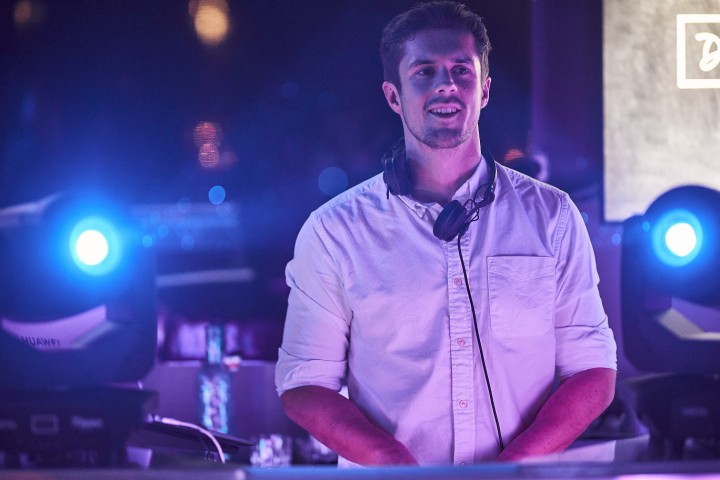 DJ in weißem Hemd mit Lichtern im Hintergrund beim Auflegen