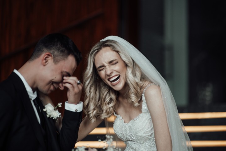 Braut und Bräutigam lachen ausgelassen wegen einer lustigen Hochzeitsüberraschung.